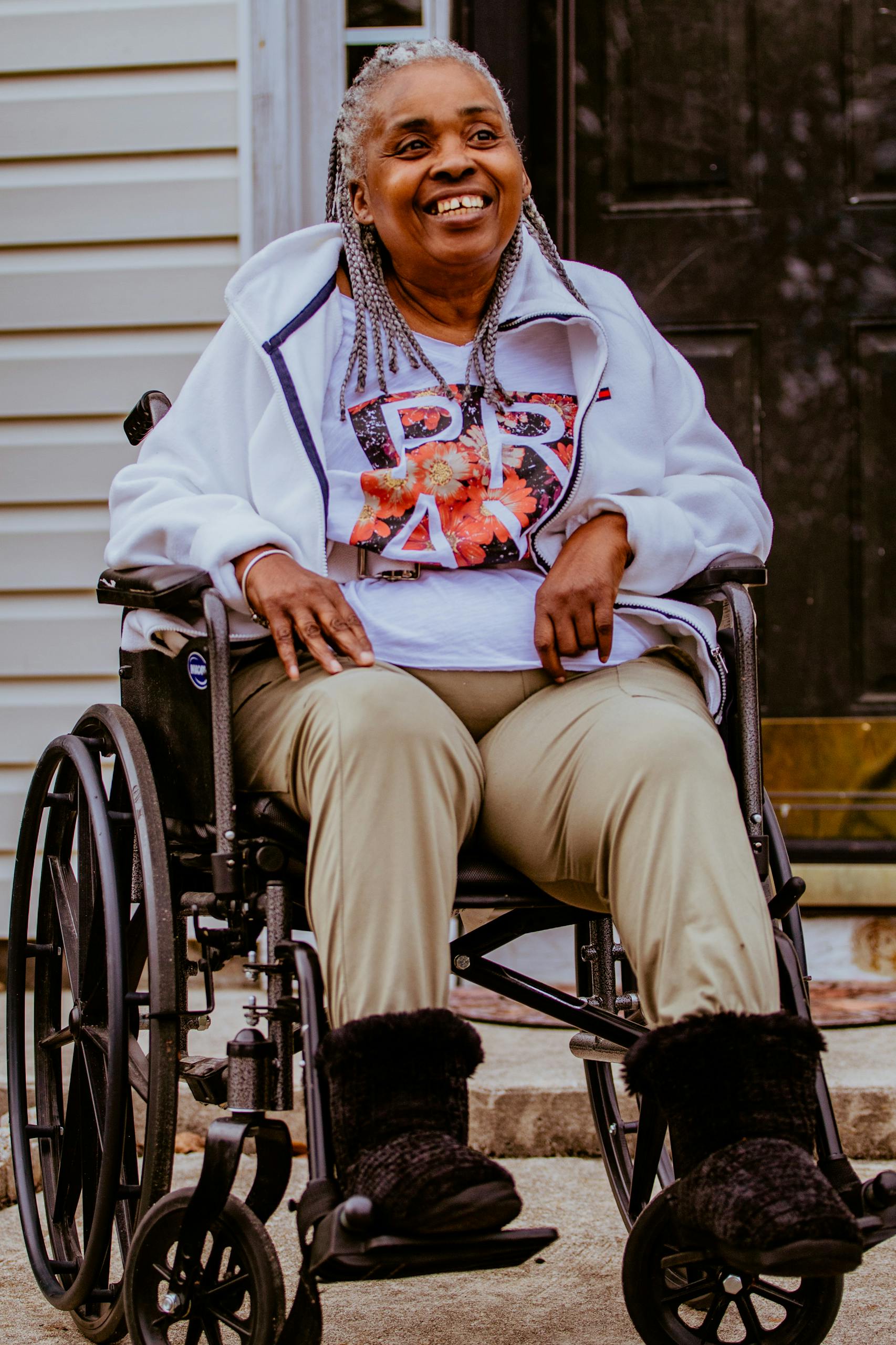 Happy elderly woman with braided hair sitting in a wheelchair, smiling brightly outside.